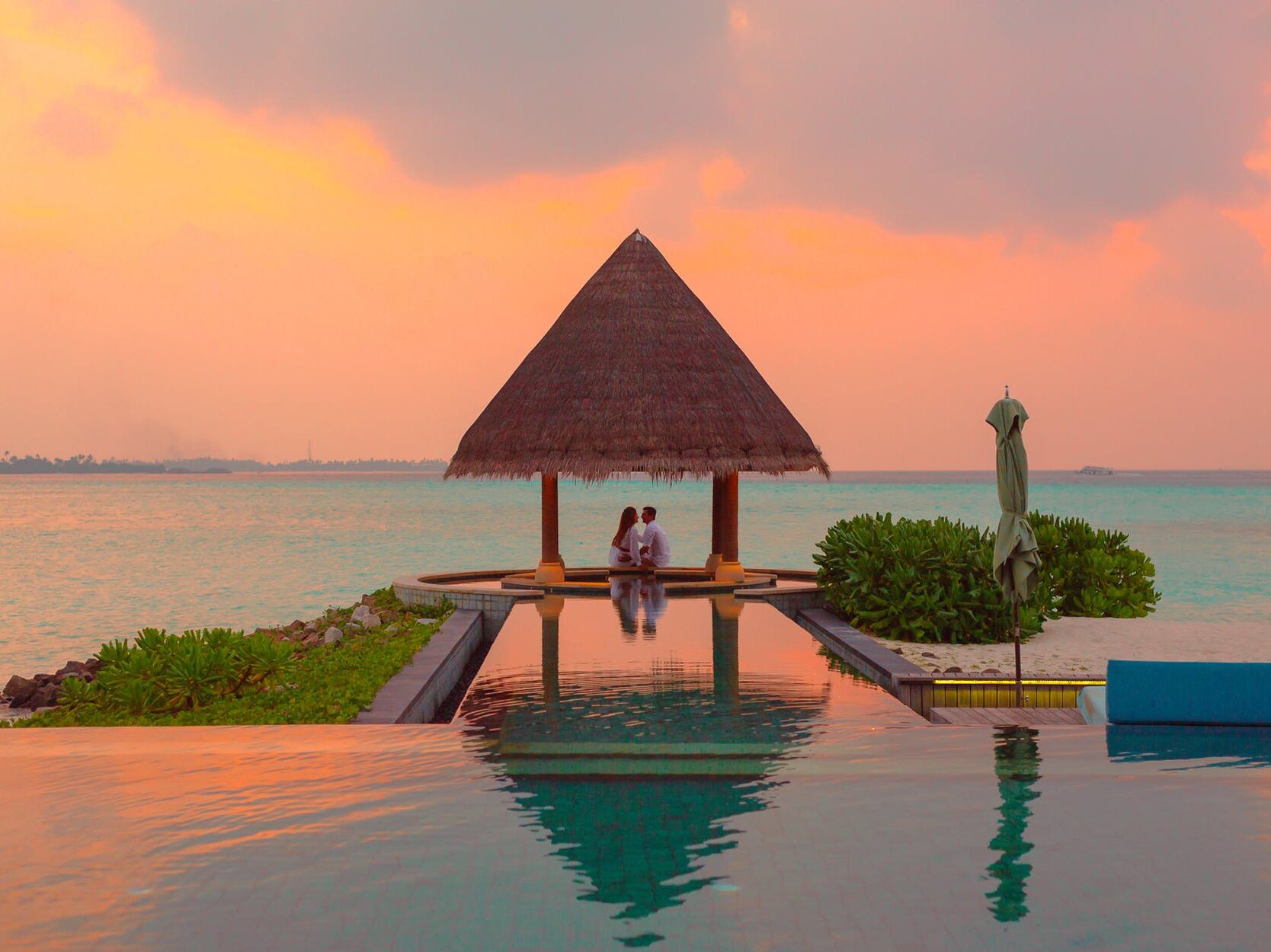 couple under hut beside sea and infinity pool