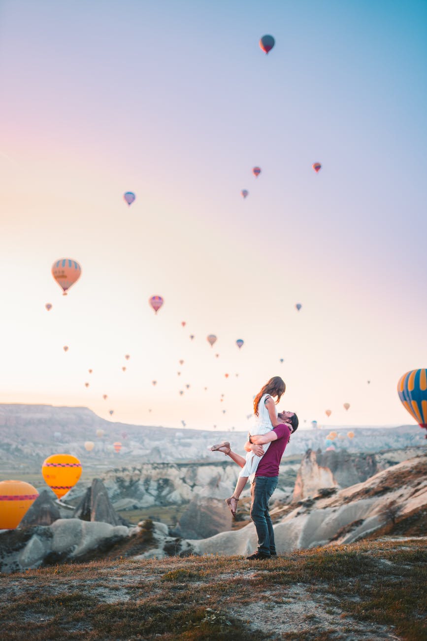 man carrying woman with hot air balloons background